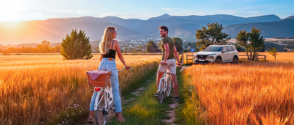 Una pareja en bici en el campo junto a un vehículo Nissan